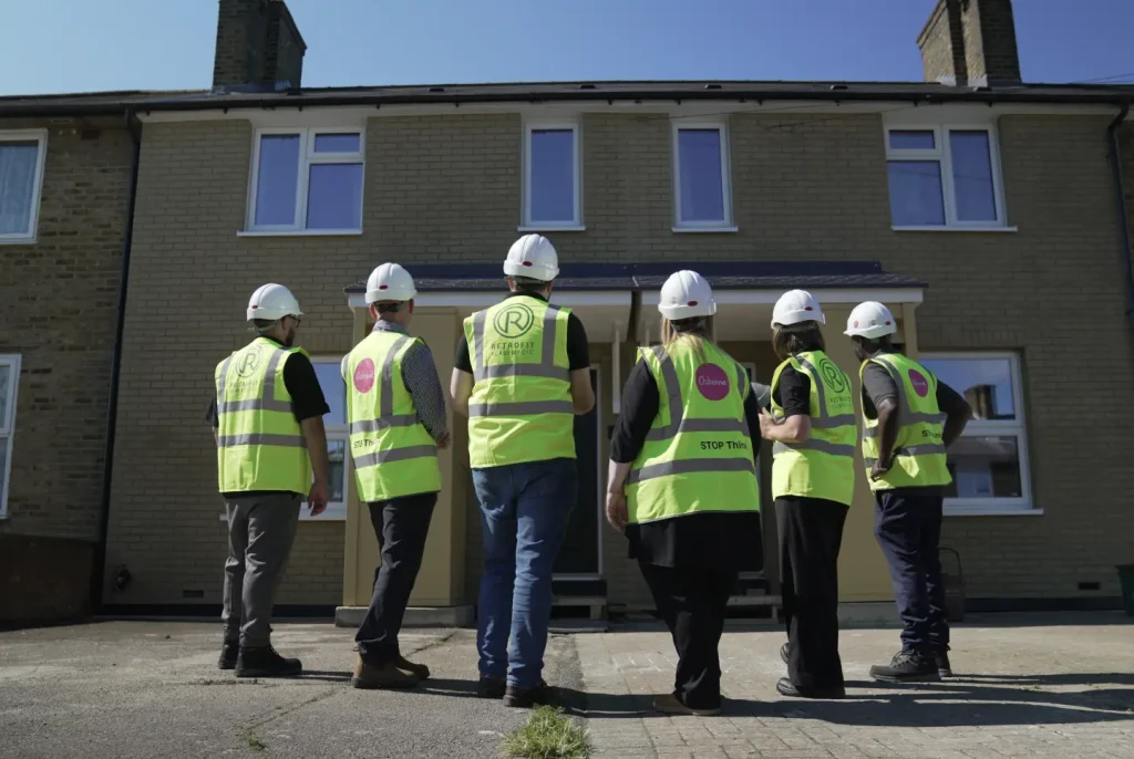 Construction workers all wearing hard hats and hi-vis staring at a house.